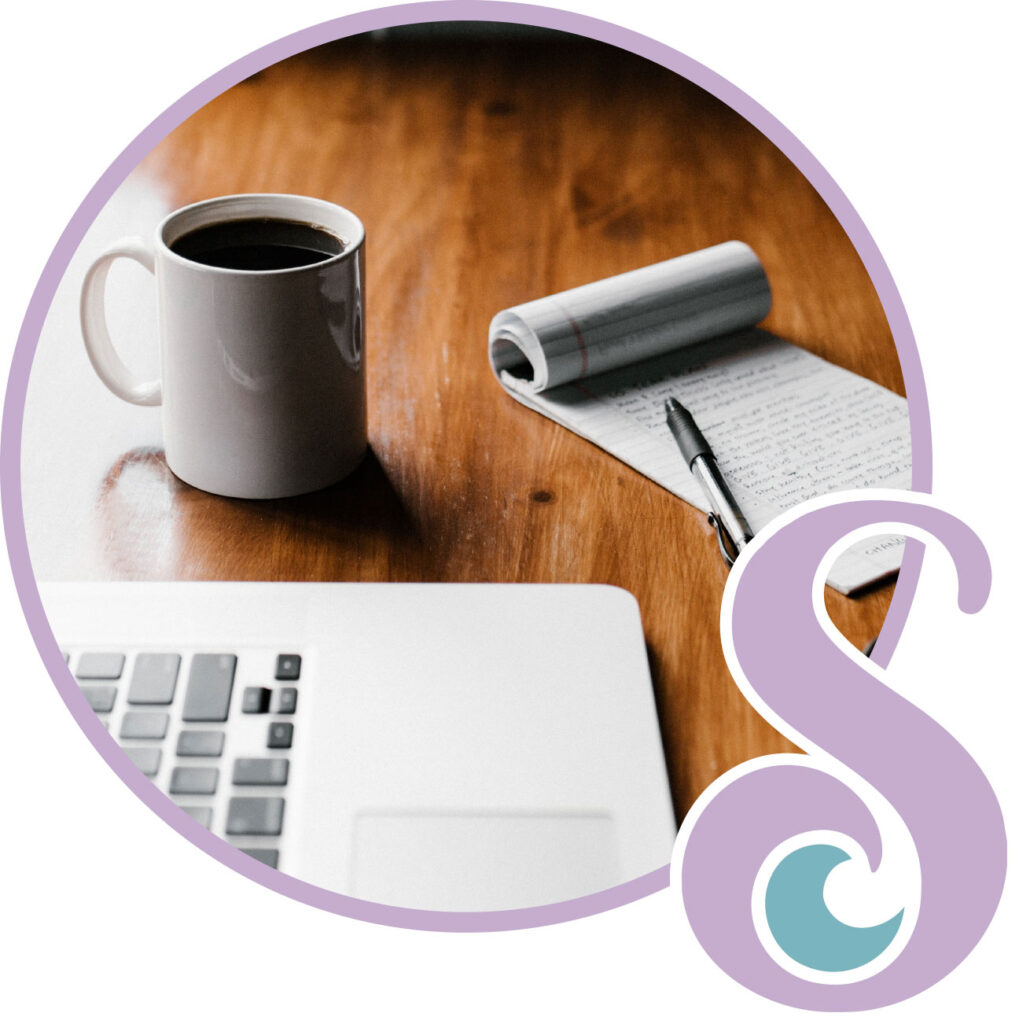 A coffee mug and a notepad on a desk with a laptop